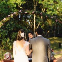 marina celebrando casamento sorrindo com microfone na mão. Aparecem os noivos de braços dados de frente pra ela